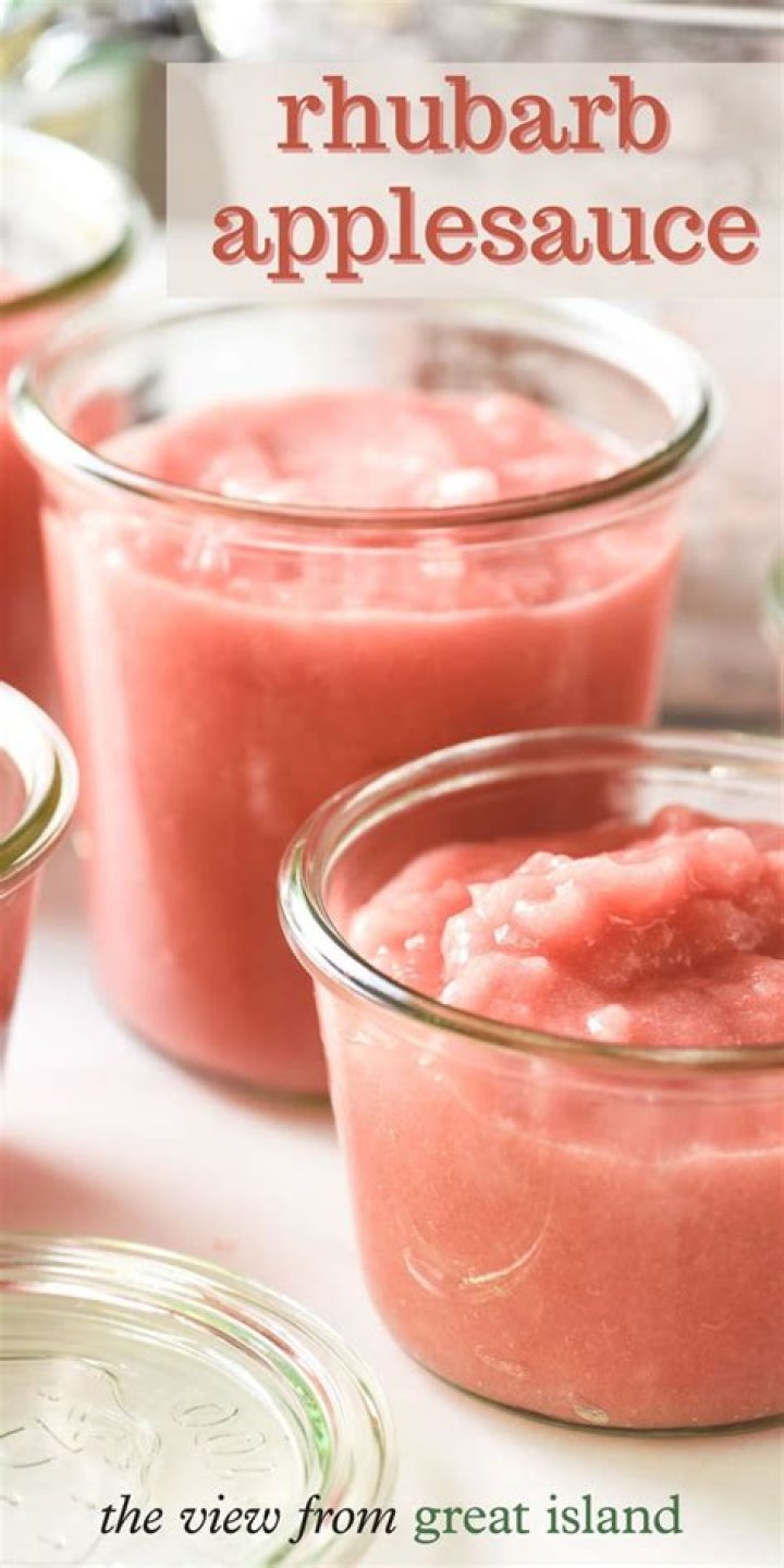 Pink applesauce in a glass jar with a wooden spoon.